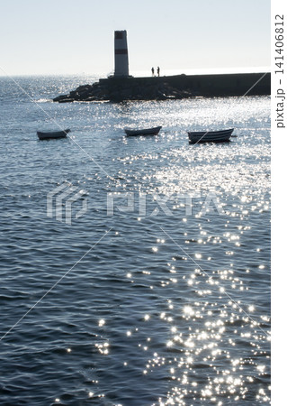 Small boats near lighthouse shimmering under bright afternoon sunlight Small boats near lighthouse shimmering under bright afternoon sunlight 141406812