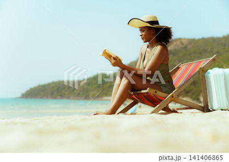 Relaxed woman in swimwear reading on a sandy seashore 141406865