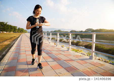 Young Asian woman checking her smartwatch while exercising at a riverside park Young Asian woman checking her smartwatch while exercising at a riverside park 141406896