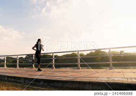 Happy Asian woman jogging along a scenic riverside pathway 141406898
