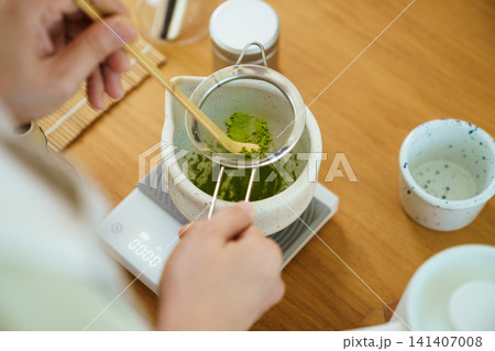 Person sifting vibrant green matcha powder during a tea preparation session Person sifting vibrant green matcha powder during a tea preparation session 141407008