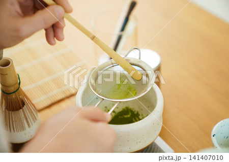 Person sifting vibrant green matcha powder during a tea preparation session Person sifting vibrant green matcha powder during a tea preparation session 141407010
