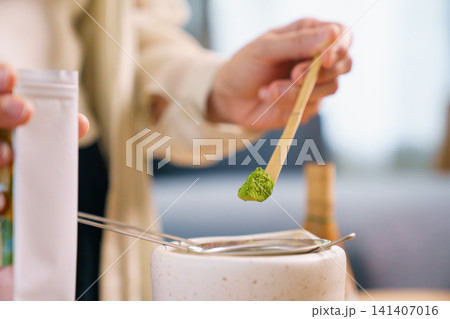 Close up of hand using traditional bamboo scoop to measure matcha powder over strainer Close up of hand using traditional bamboo scoop to measure matcha powder over strainer 141407016