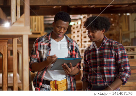 Diverse young craftsmen working together and reviewing plans in lumber mill Diverse young craftsmen working together and reviewing plans in lumber mill 141407176