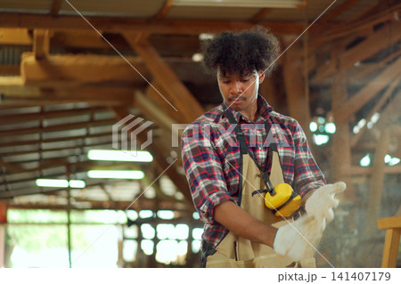 Young carpenter shaking sawdust off protective gloves in workshop 141407179