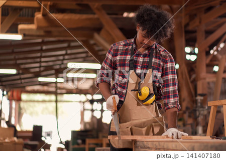 carpenter using a hand saw to cut wood in a workshop carpenter using a hand saw to cut wood in a workshop 141407180