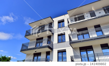 Contemporary urban apartment block with protruding balconies, white and grey facade contrast and reflective windows under a bright sky. 141409802