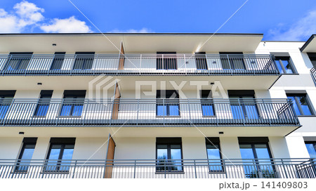 Contemporary urban apartment block with protruding balconies, white and grey facade contrast and reflective windows under a bright sky. Contemporary urban apartment block with protruding balconies, white and grey facade contrast and reflective windows under a bright sky. 141409803