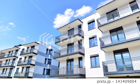 Contemporary urban apartment block with protruding balconies, white and grey facade contrast and reflective windows under a bright sky. Contemporary urban apartment block with protruding balconies, white and grey facade contrast and reflective windows under a bright sky. 141409804