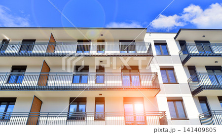 Contemporary urban apartment block with protruding balconies, white and grey facade contrast and reflective windows under a bright sky. Contemporary urban apartment block with protruding balconies, white and grey facade contrast and reflective windows under a bright sky. 141409805