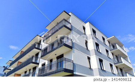 Contemporary urban apartment block with protruding balconies, white and grey facade contrast and reflective windows under a bright sky. 141409812