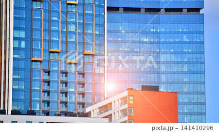 A low-rise residential building stands against a backdrop of tall glass buildings. An urban quarter of modern architecture. A low-rise residential building stands against a backdrop of tall glass buildings. An urban quarter of modern architecture. 141410296