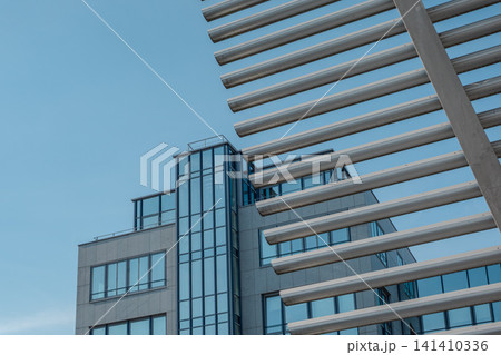 Modern glass office building facade near Hackerbruecke in Munich, Bavaria, with metal sunshade structure and green trees in foreground 141410336