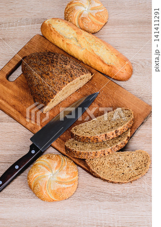 Different breeds on wooden background. Knife on a wooden board with bread and different buns on the table. 141411291