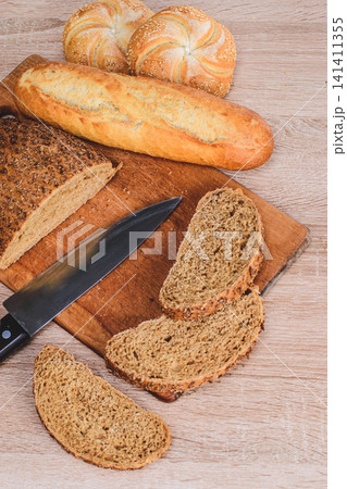 Different breeds on wooden background. Knife on a wooden board with bread and different buns on the table Different breeds on wooden background. Knife on a wooden board with bread and different buns on the table 141411355