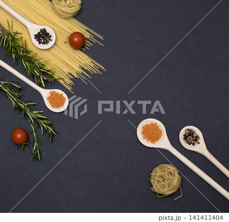 Italian food ingredients.Still life of cooking pasta on a black background top view. Wooden spoons with spices. Frame of products and vegetables. 141411404