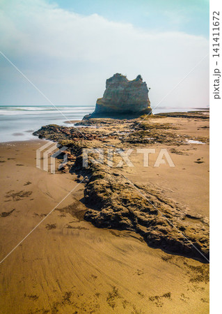 Aerial view of coastal rock formations rising from the sea with crashing waves and sandy beach in Indonesia 141411672