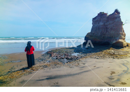 Aerial view of coastal rock formations rising from the sea with crashing waves and sandy beach in Indonesia 141411681