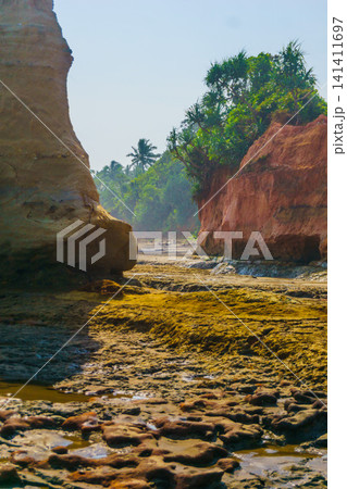 Aerial view of coastal rock formations rising from the sea with crashing waves and sandy beach in Indonesia 141411697