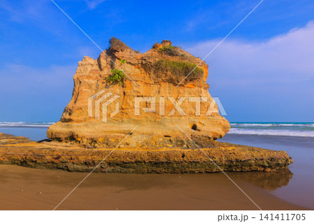 Aerial view of coastal rock formations rising from the sea with crashing waves and sandy beach in Indonesia 141411705
