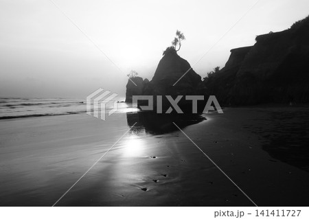 Aerial view of coastal rock formations rising from the sea with crashing waves and sandy beach in Indonesia 141411727