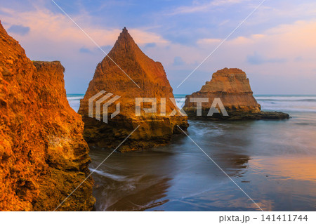 Aerial view of coastal rock formations rising from the sea with crashing waves and sandy beach in Indonesia Aerial view of coastal rock formations rising from the sea with crashing waves and sandy beach in Indonesia 141411744