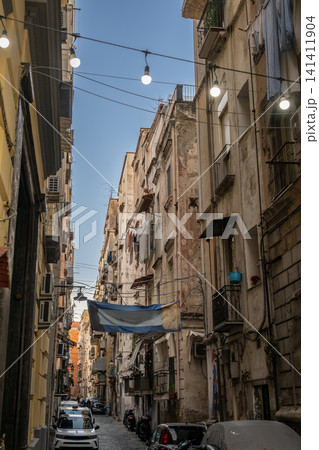 Naples, italy. December 29, 2024. Buildings lining a narrow street in the historic center of naples, italy, with laundry drying on balconies and string lights overhead Naples, italy. December 29, 2024. Buildings lining a narrow street in the historic center of naples, italy, with laundry drying on balconies and string lights overhead 141411904