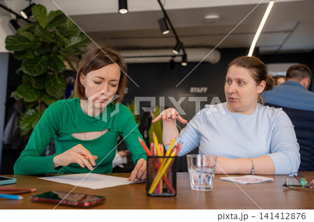 Women working with pencils and paper, analyzing and strategizing at cafe counter workspace. Analyzing, strategizing, pencils, counter, workspace. Women working with pencils and paper, analyzing and strategizing at cafe counter workspace. Analyzing, strategizing, pencils, counter, workspace. 141412876