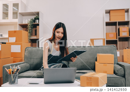 Startup SME small business entrepreneur of freelance Asian woman wearing apron using laptop and box to receive and review orders online to prepare to pack sell to customers, online sme business ideas. Startup SME small business entrepreneur of freelance Asian woman wearing apron using laptop and box to receive and review orders online to prepare to pack sell to customers, online sme business ideas. 141412930