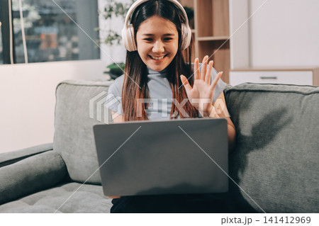 Beautiful young asian woman sitting on sofa and holding joystick playing online video game in living room at house Beautiful young asian woman sitting on sofa and holding joystick playing online video game in living room at house 141412969