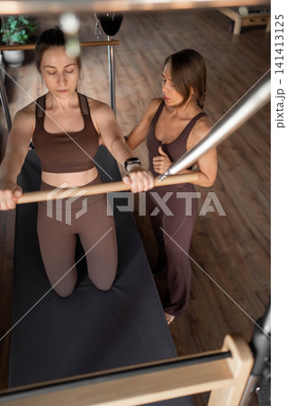 Elegant pilates pair performing synchronized deep stretches using reformer beds in bright wood-floored studio. Synchronized, deep stretch, reformer, studio, wood floor Elegant pilates pair performing synchronized deep stretches using reformer beds in bright wood-floored studio. Synchronized, deep stretch, reformer, studio, wood floor 141413125
