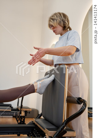 Woman training pilates with trainer on the reformer bed. Reformer pilates studio machine for fitness workouts in gym. Fit, healthy and strong authentical body. Fitness Woman training pilates with trainer on the reformer bed. Reformer pilates studio machine for fitness workouts in gym. Fit, healthy and strong authentical body. Fitness 141413174