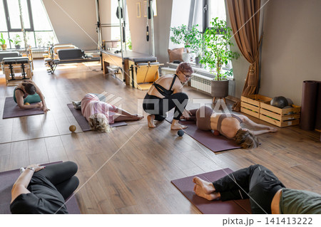 Woman instructor teaching mobility to a group of seniors in a pilates studio. Group of senior people exercising on mats to improve balance and flexibility. Healthy lifestyle and wellness Woman instructor teaching mobility to a group of seniors in a pilates studio. Group of senior people exercising on mats to improve balance and flexibility. Healthy lifestyle and wellness 141413222