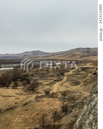 View of arid valley landscape with dirt road and scattered trees near river. View of arid valley landscape with dirt road and scattered trees near river. 141413400