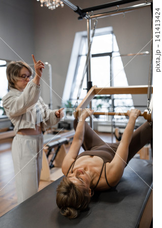 Woman doing pilates exercises on Balanced Body Cadillac machine at studio, focusing on strength and flexibility 141413424