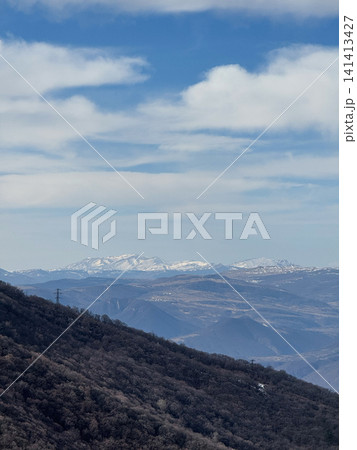 Snow-capped mountains in distance viewed beyond forested ridge and cloudy sky. Snow-capped mountains in distance viewed beyond forested ridge and cloudy sky. 141413427
