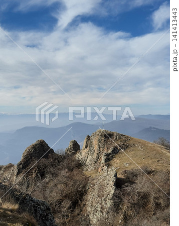 Mountain ridge with cross and misty valleys under bright blue cloudy sky. 141413443