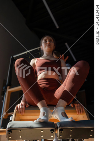 Foot work and core exercise on a Pilates Reformer machine illuminated by sunlight. Fit, healthy and strong authentical body. Fitness concept. 141413464