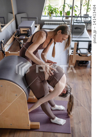 Young caucasian woman doing roll down exercise in a pilates bright studio. Their workout focuses on core strength and flexibility in a modern fitness environment. Young caucasian woman doing roll down exercise in a pilates bright studio. Their workout focuses on core strength and flexibility in a modern fitness environment. 141413484
