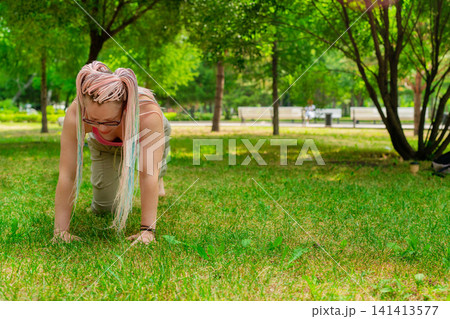 Yoga instructor demonstrating cat-cow pose on mat outdoors in green summer park for students. Cat-cow pose, yoga, instructor, mat, summer, outdoors. Yoga instructor demonstrating cat-cow pose on mat outdoors in green summer park for students. Cat-cow pose, yoga, instructor, mat, summer, outdoors. 141413577
