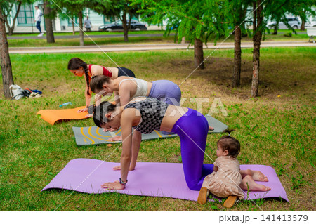 Women in sportswear demonstrating cat-cow pose on mats with children during outdoor yoga class. Cat-cow pose, yoga, mats, children, outdoors. Women in sportswear demonstrating cat-cow pose on mats with children during outdoor yoga class. Cat-cow pose, yoga, mats, children, outdoors. 141413579