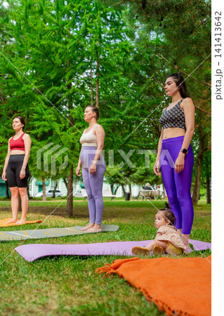 Ladies in purple leggings and green tops standing and stretching before group yoga class in summer park. Purple leggings, stretching, group, yoga, park. Ladies in purple leggings and green tops standing and stretching before group yoga class in summer park. Purple leggings, stretching, group, yoga, park. 141413642