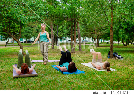 Yoga instructor and group raising arms and stretching during active outdoor fitness practice on mats. Stretching, yoga instructor, mats, arms, outdoor. 141413732