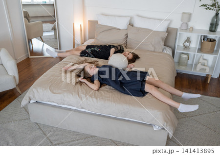 Girl reading and lying down with blanket on bed in softly lit modern bedroom. Lying, blanket, bed, reading, modern, girl. 141413895