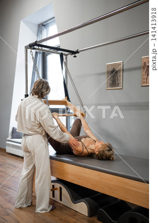 Pilates mature woman doing back strengthening exercises on in pilates studio. Balanced Body Cadillac machine for fitness workouts in gym. Fit, healthy and strong authentical body. Fitness concept. 141413918