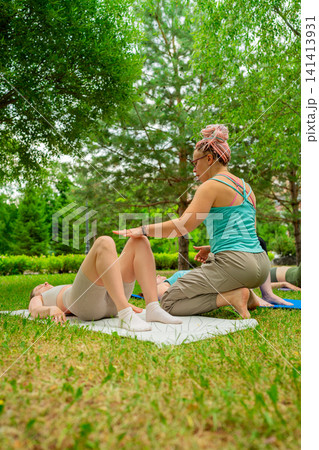 Instructor helping women in leg and abs stretches during group yoga session in the park. Stretches, yoga, instructor, park, group, abs. Instructor helping women in leg and abs stretches during group yoga session in the park. Stretches, yoga, instructor, park, group, abs. 141413931