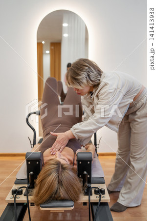 Woman training on the reformer bed at Glute bridge Pilates workout. Reformer pilates studio machine for fitness workouts in gym. Fit, healthy and strong authentical body. Fitness concept 141413938