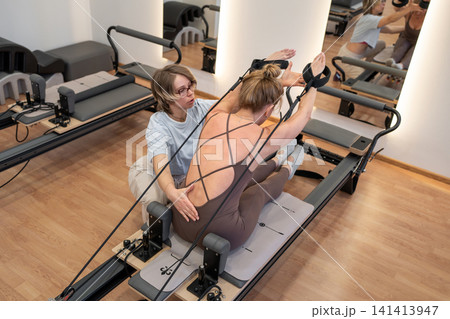 A woman in activewear does pilates exercises for the chest and back muscles with a reformer machine in a sunlite studio, committed to her workout routine 141413947