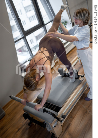 Woman training pilates with trainer on the reformer bed. Reformer pilates studio machine for fitness workouts in gym. Fit, healthy and strong authentical body. Fitness Woman training pilates with trainer on the reformer bed. Reformer pilates studio machine for fitness workouts in gym. Fit, healthy and strong authentical body. Fitness 141413948
