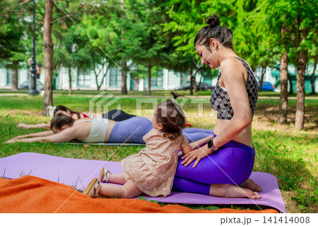 Happy mother and daughter connecting and relaxing on yoga mats after workout in summer park. Relaxing, yoga, mother, daughter, workout, park. Happy mother and daughter connecting and relaxing on yoga mats after workout in summer park. Relaxing, yoga, mother, daughter, workout, park. 141414008